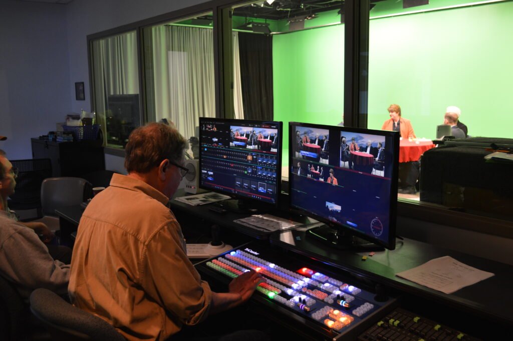 Media production control room looking into green screen studio