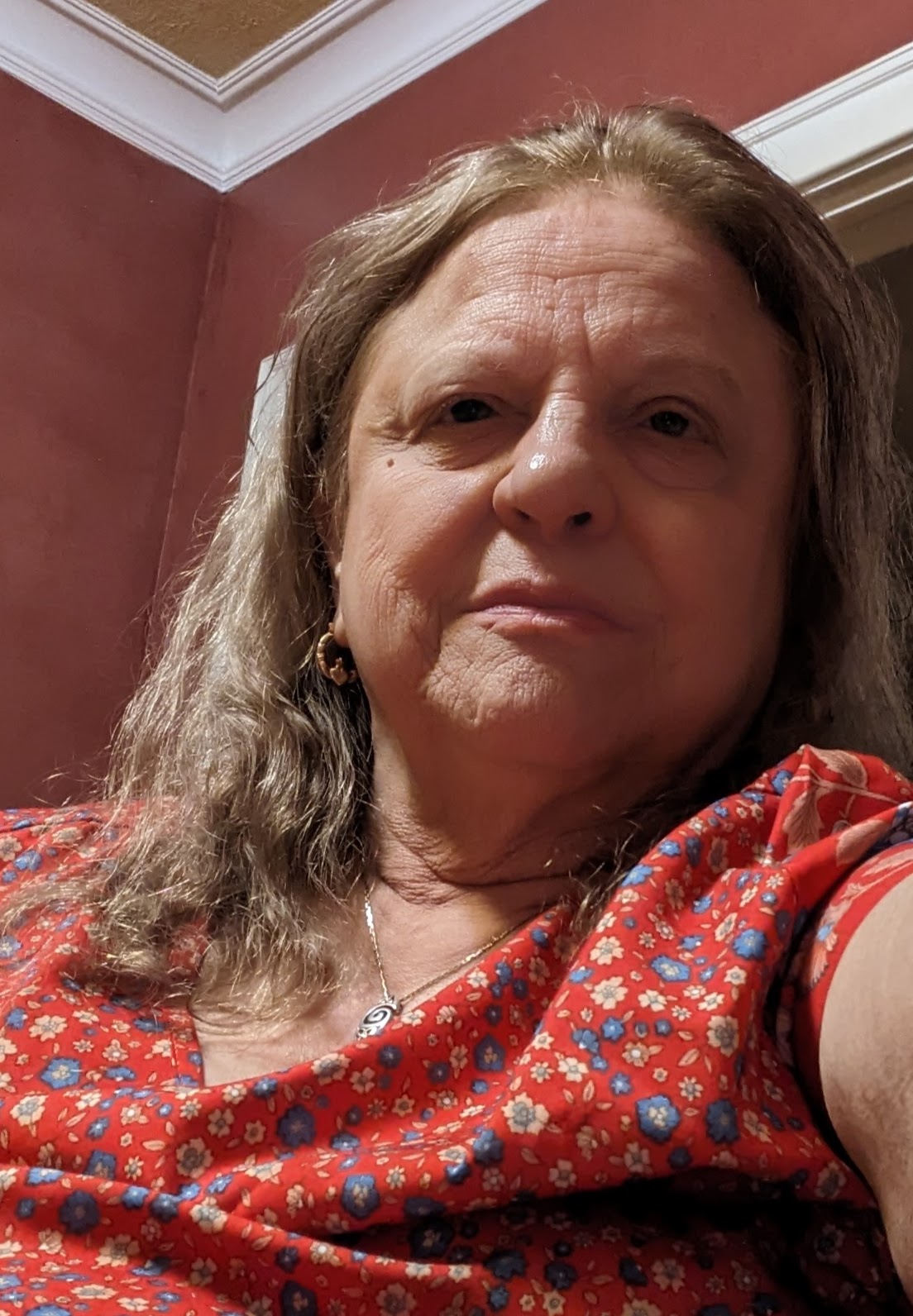 A photo of Lorene, a woman with shoulder length blonde hair and wearing a red floral patterned shirt with a necklace.