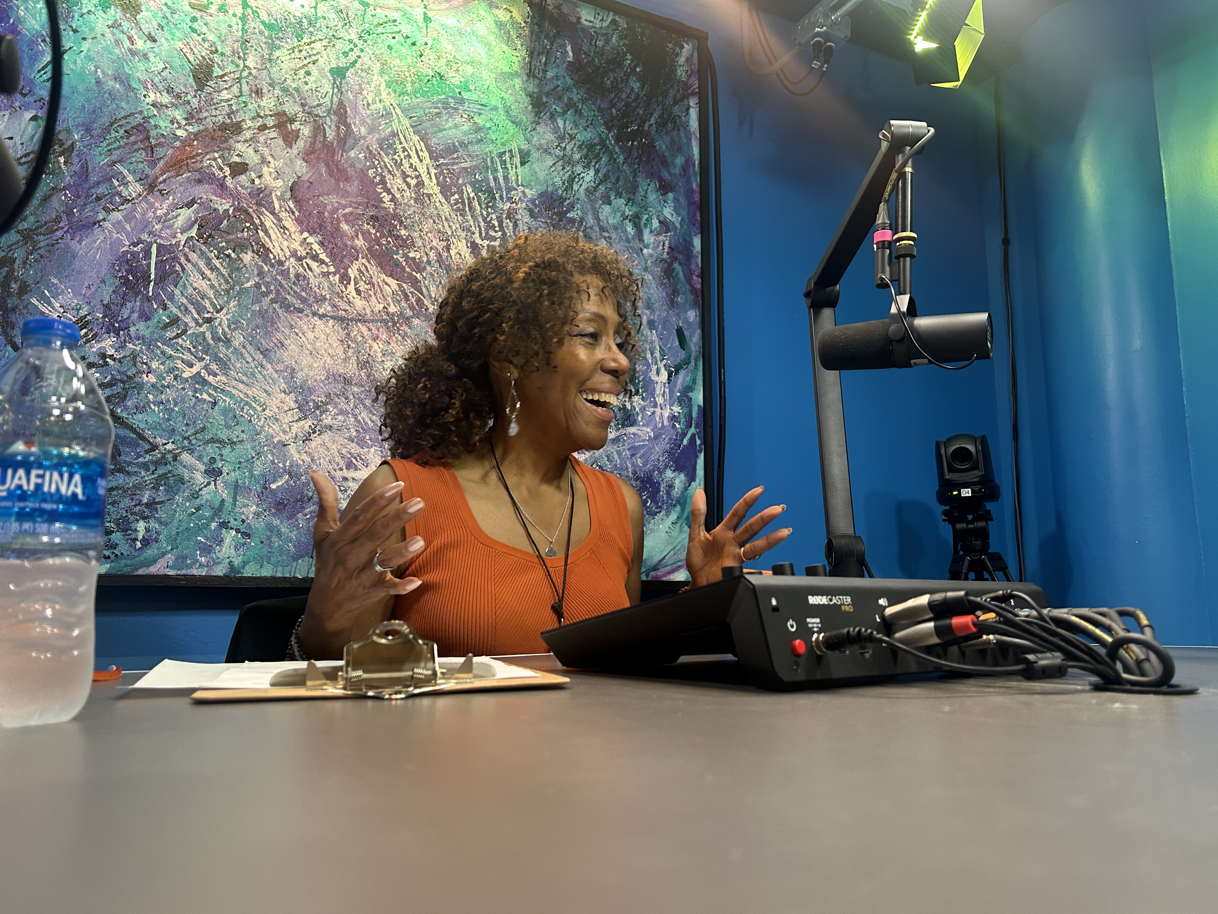 Marvinetta, laughing and gesturing with her hands, sits in the Vidcast Studio in front of a microphone.