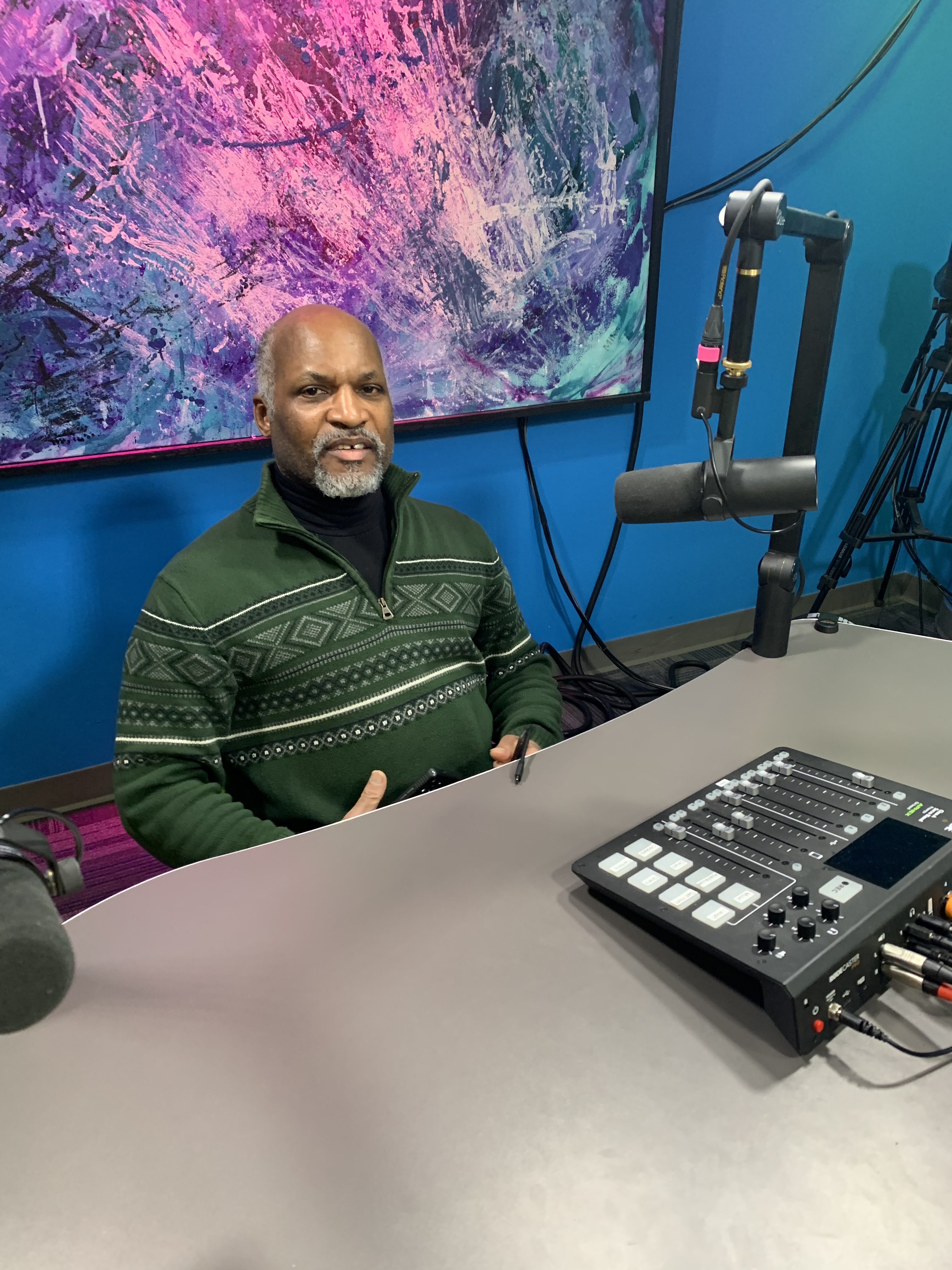 Raven Allen sits in the vidcast studio in front of a microphone at Public Media Network